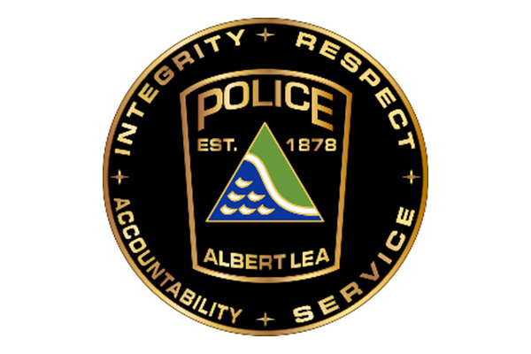 Albert Lea Police Department badge with gold border, featuring a shield, a green triangle with water waves, and the words 
