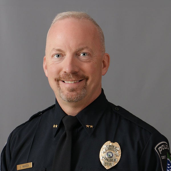 Darren Hanson, A man in a police uniform stands in front of a gray background, wearing a badge and insignia on his shirt.
