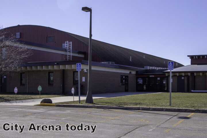 A large brick and metal arena building with accessible parking signs in front; text reads 