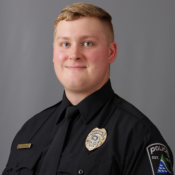 Ben Witham, A uniformed police officer with a badge and name tag smiles slightly in front of a plain gray background.