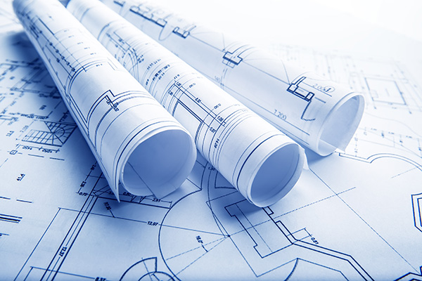 Three rolled architectural blueprints rest on top of unrolled building plans, showing technical drawings and floor layouts.