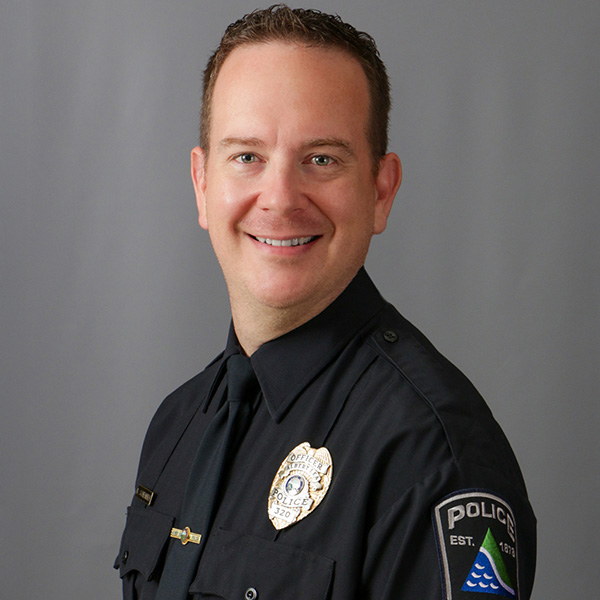 Brian Schember, A police officer in uniform smiles at the camera against a gray background.