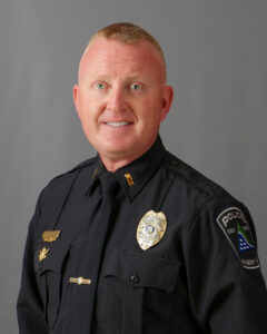 A police officer in uniform poses for a professional portrait against a plain gray background.