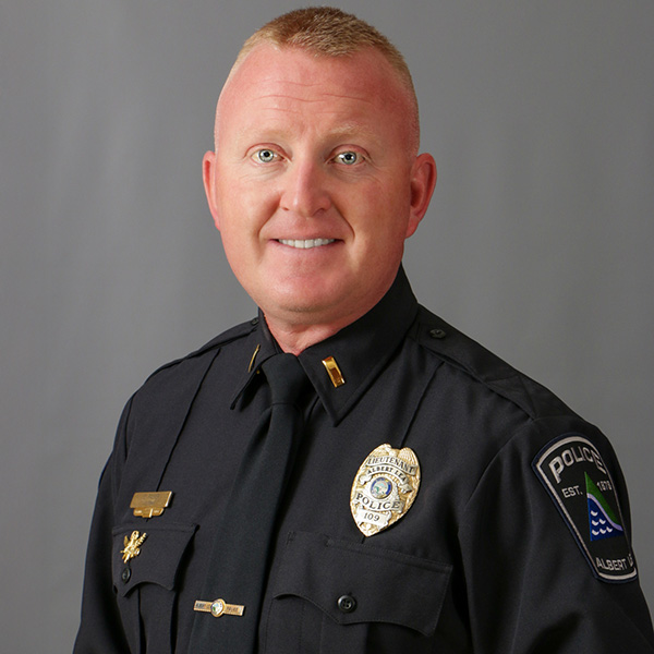 Darin Palmer, A person in a police uniform stands against a gray background.
