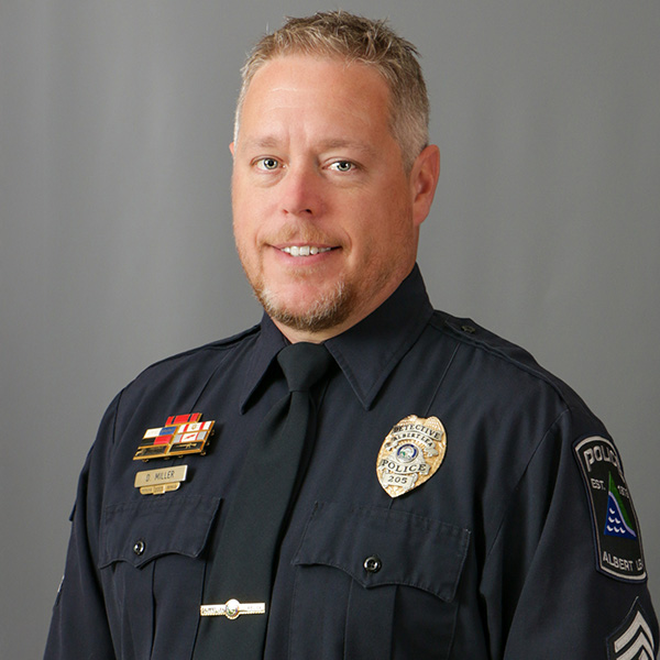 David Miller, A man in a police uniform with badges smiles against a plain background.