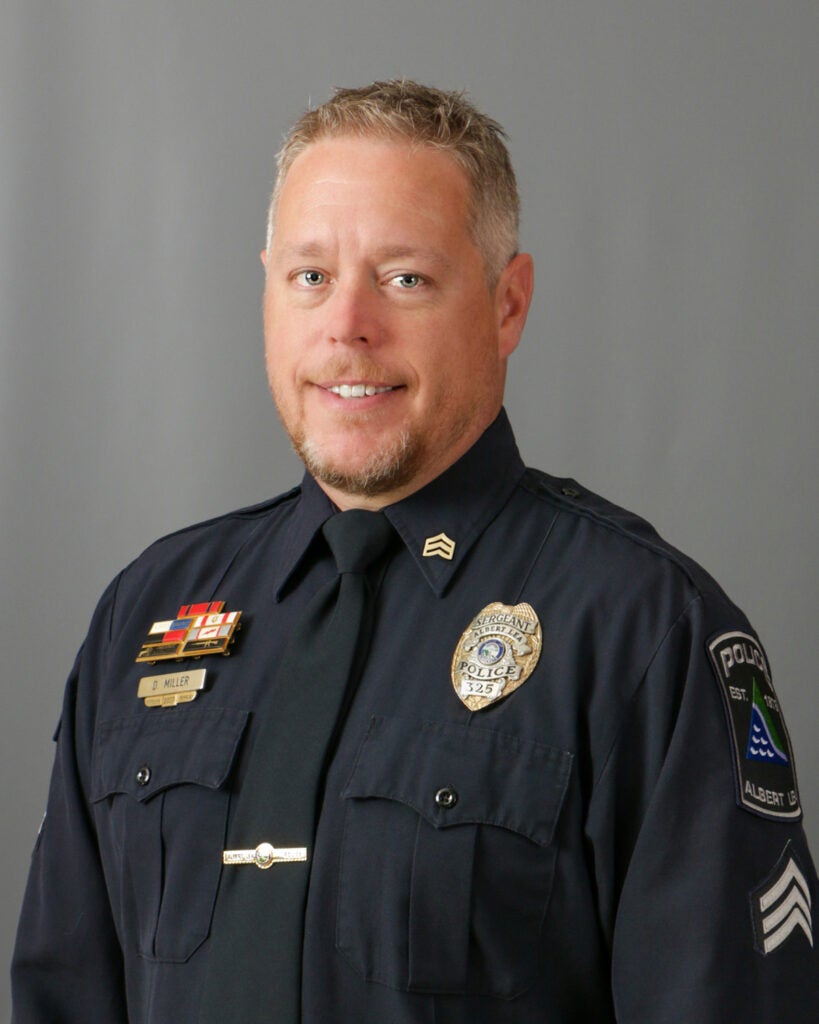 David Miller, A man in a police uniform with badges smiles against a plain background.