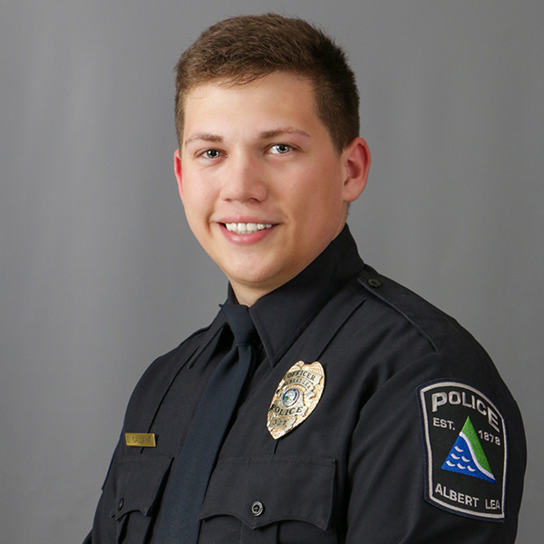 Dylan Callahan, A person in a police uniform with badges, smiling against a gray background.