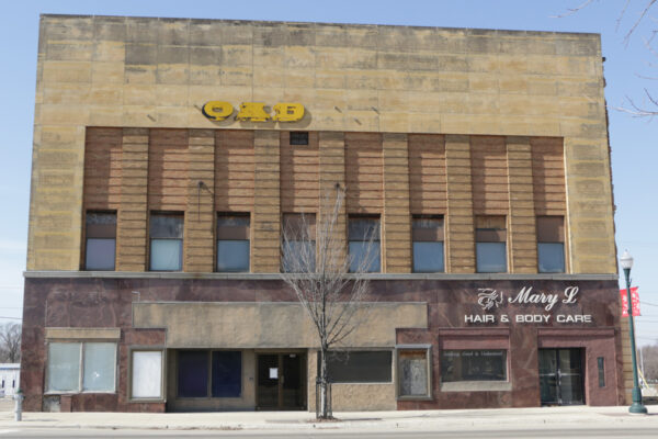 A two-story building with a faded upper facade, partially visible yellow letters, and a ground-floor business called 