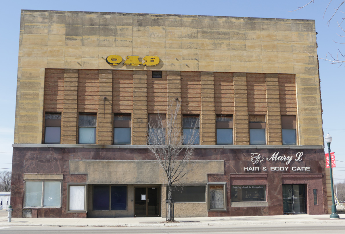 A two-story building with a faded upper facade, partially visible yellow letters, and a ground-floor business called