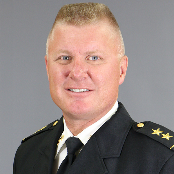 JD Carlson, A man in a formal black uniform with gold stars on the shoulders poses against a plain gray background.