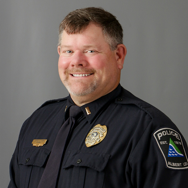 Jeff Strom, Smiling police officer in uniform with badges, standing against a gray background.