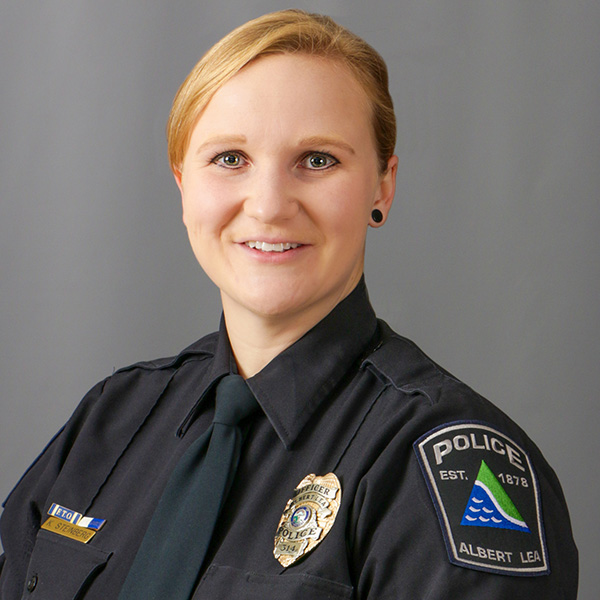 Kristen Steinberg, Police officer in uniform poses against a gray background, smiling. The uniform has an Albert Lea patch and a badge.