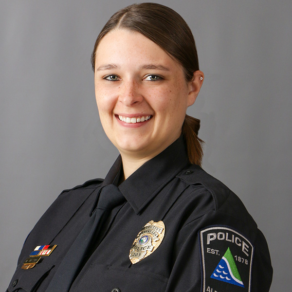 Megan Wilson, Smiling police officer in uniform with badges, against a gray background.