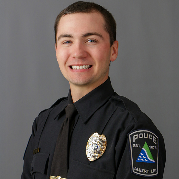 Tyler Lair, A person in a police uniform smiling against a plain background. The uniform features badges and a patch that reads "Albert Lea Police.