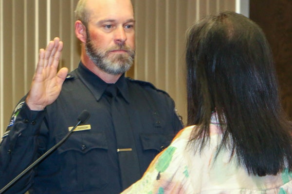 Police officer in uniform stands with his right hand up in front of a woman giving the oath of office