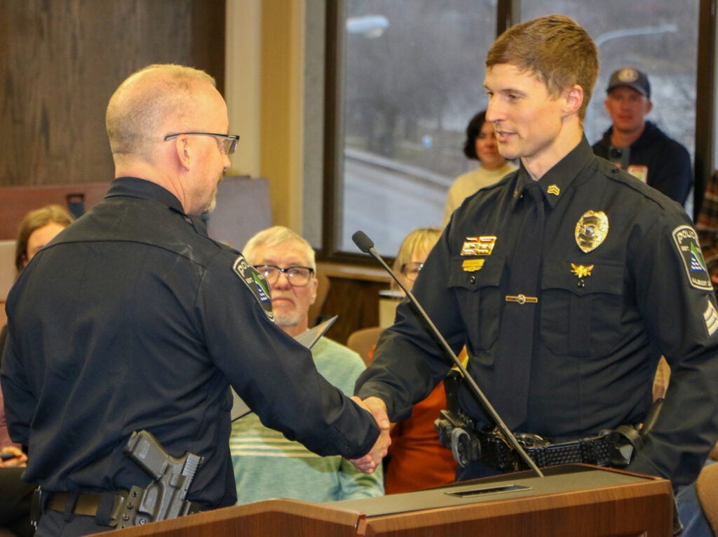 One police officer shakes the hand of another at a meeting