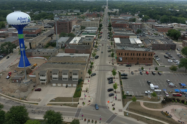 An aerial shot shows a small city with a tall, blue and green water tower on the left, emblazoned with 