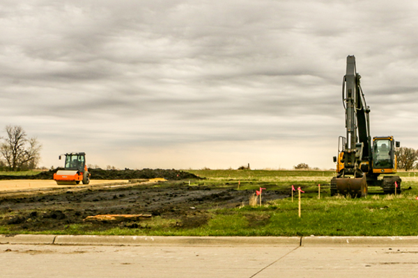 Construction land with heavy machinery including an excavator and a roller, under a cloudy sky