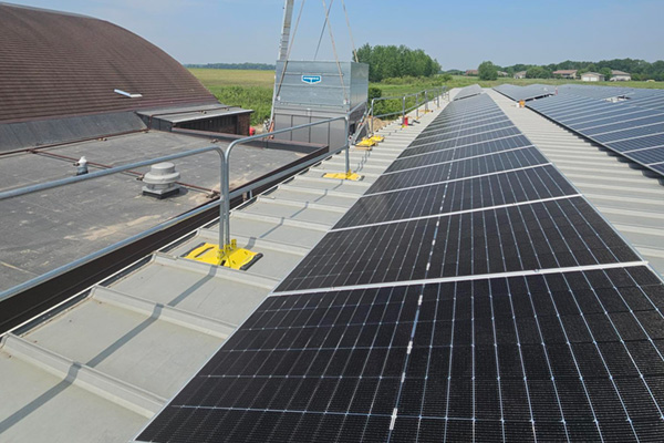 A high-angle shot shows a rooftop solar panel installation, with a long row of dark solar panels extending from the foreground into the distance on the right side of the frame.