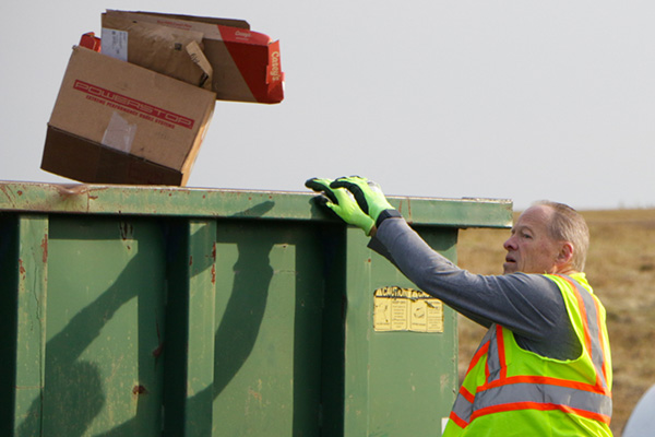 A worker at the transfer station throws away garbage into a green dumpster.